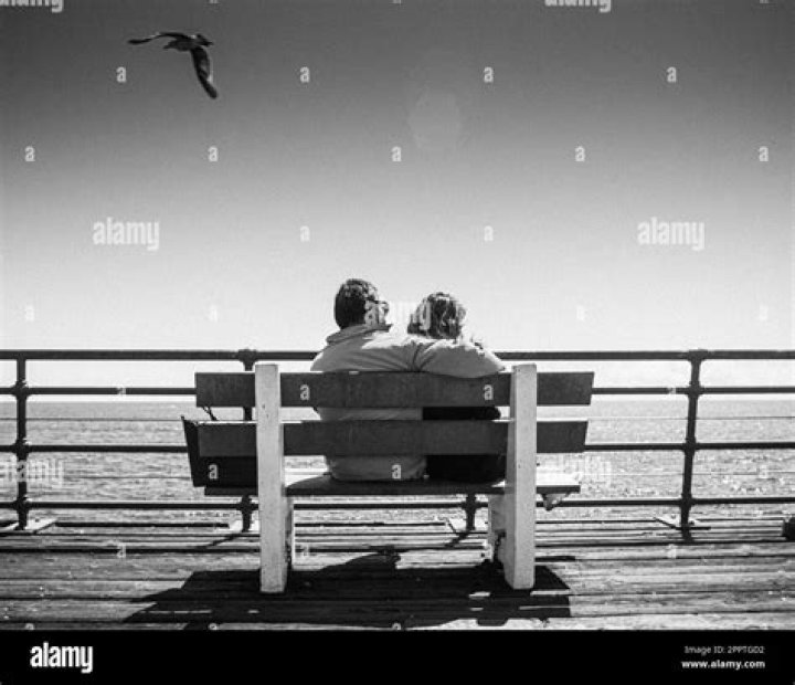 a man and woman sitting next to each other holding coffee cups in front